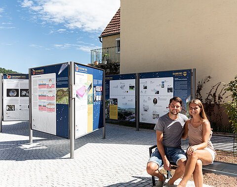 Ein Mann und eine Frau sitzen auf einer Bank bei mehreren Informationstafeln über den Geopark Ries.