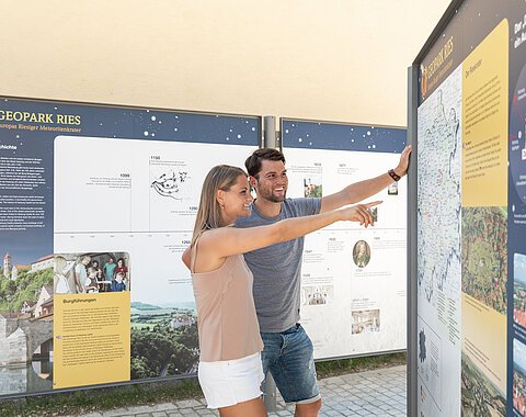 Ein Mann und eine Frau betrachten eine Informationstafel über den Geopark Ries.