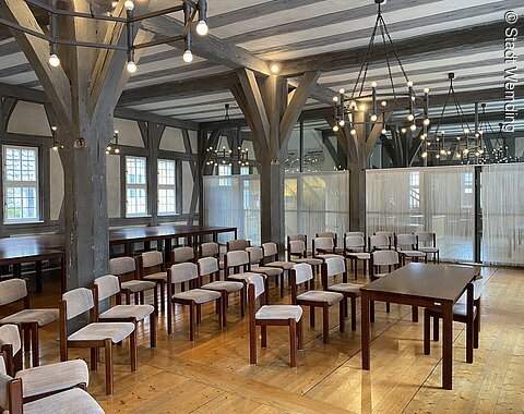 Blick in einen festlich beleuchteten Saal mit Holzboden und historischem Ambiente.