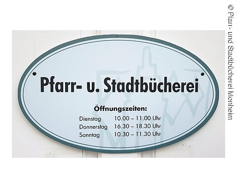 Pfarr- und Stadtbücherei Monheim Schild mit Öffnungszeiten der Pfarr- und Stadtbücherei, Dienstag 10-11 Uhr, Donnerstag 16:30-18:30 Uhr, Sonntag 10:30-11:30 Uhr.
