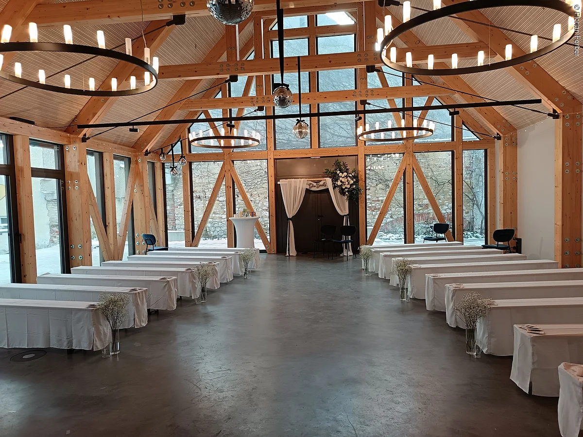 Innenraum eines Veranstaltungsraums mit Holzbalken und Tischen mit weißen Tischdecken.