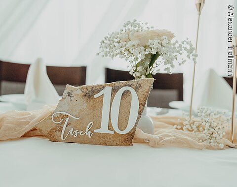 Tischnummer 10 auf Stein mit Blumen und Kerzen auf gedecktem Tisch in hellem Raum.
