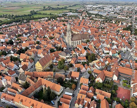 Luftaufnahme einer Stadt mit vielen roten Dächern und einer großen Kirche in der Bildmitte.
