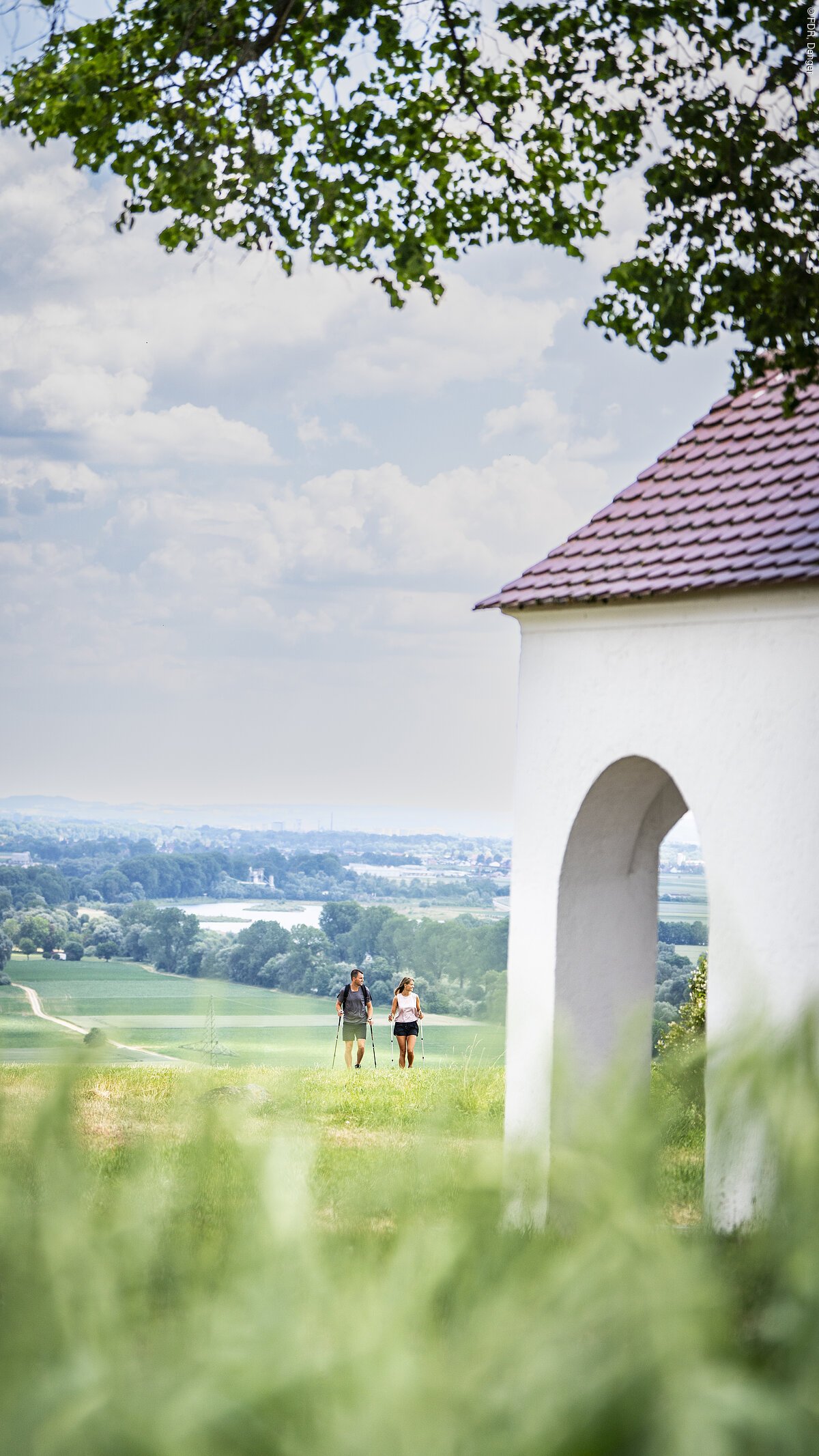 Wanderer auf dem Edelweißweg an der Kapelle in Zirgesheim Zwei Personen wandern auf einem grünen Hügel, im Hintergrund eine weite Landschaft.
