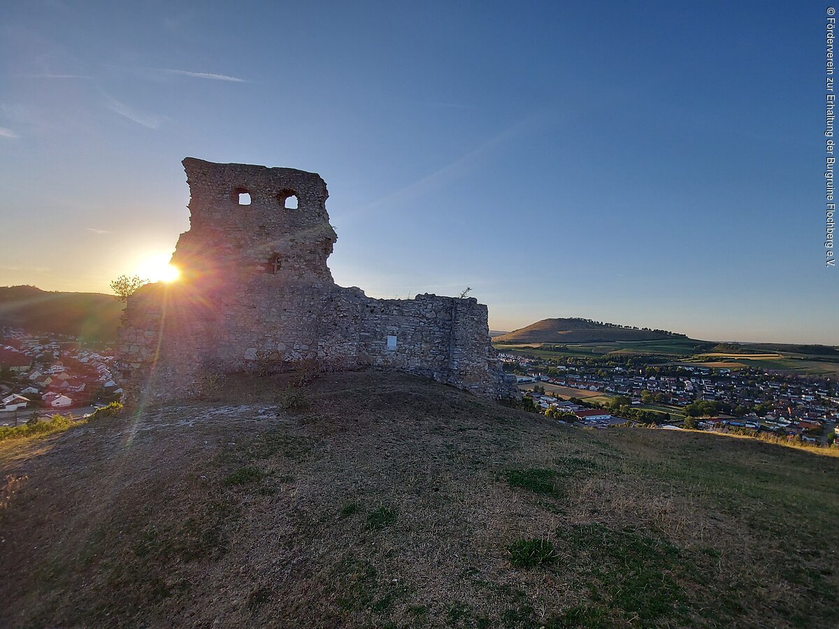 Die Sonne geht hinter der Burgruine Flochberg unter. Im Hintergrund sieht man die Stadt Bopfingen und den Ipf.