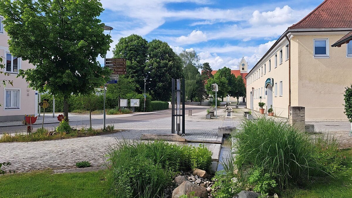 Ein teilweise begrünter Platz entlang der Hauptstraße und einem Gasthof an der Seite