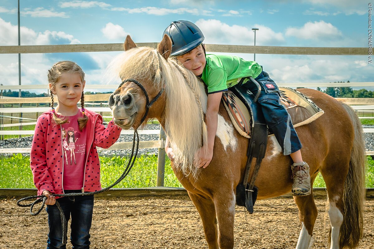 Ein Mädchen führt ein Pony auf dem ein Junge sitzt.