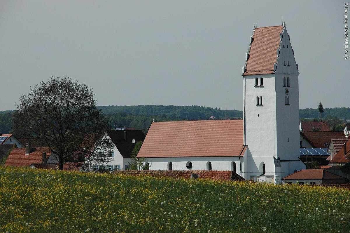 Blick auf die Kirche St. Laurentius. Im Vordergrund eine gelb blühende Wiese