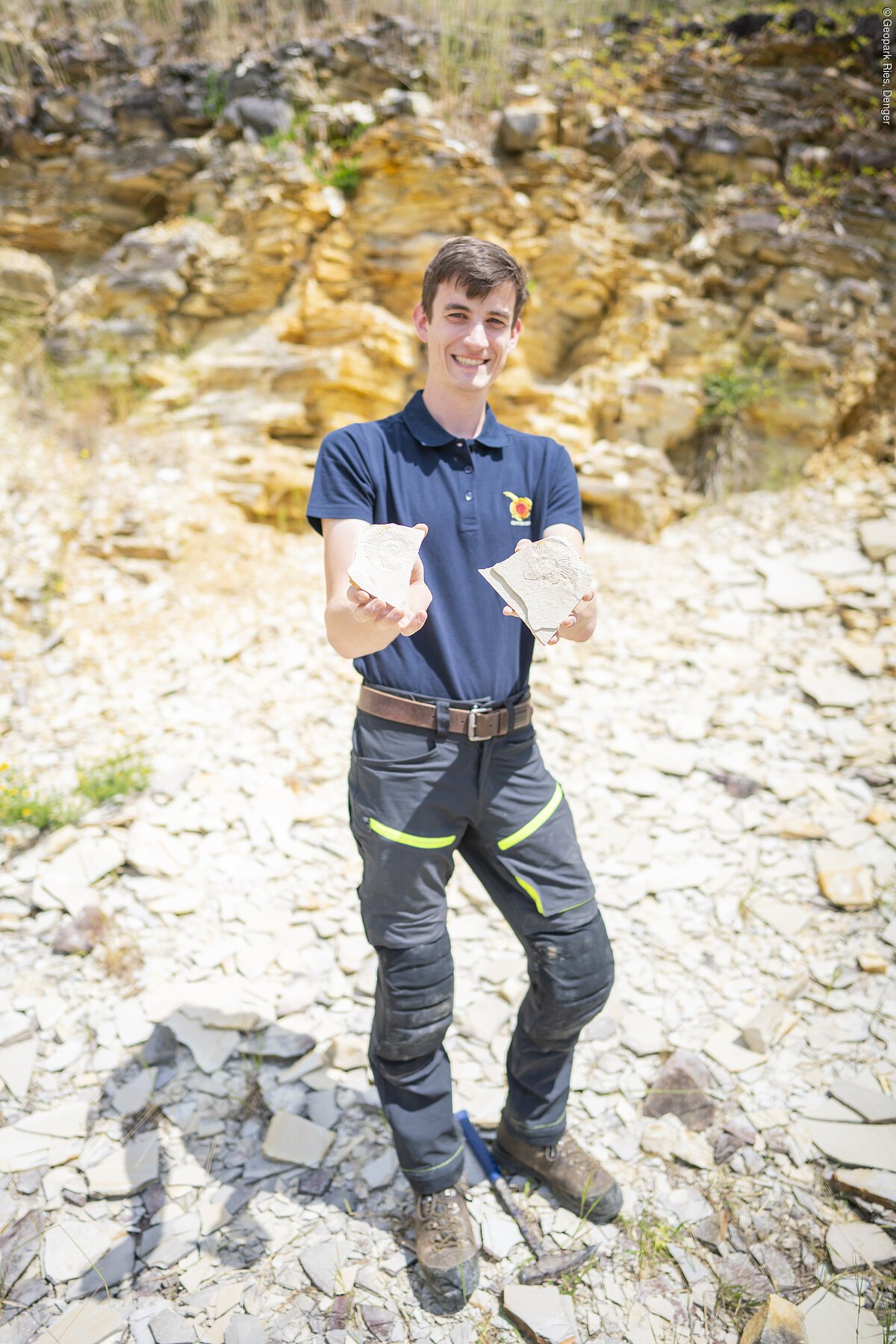 Person in Outdoorkleidung hält zwei Steine, Hintergrund aus Felsen und Geröll.