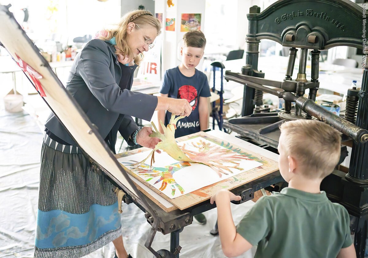 KunstMuseum Donau-Ries Die Leiterin des KunstMuseums führt zwei Jungs den Bilddruck mit einer alten Maschine vor.