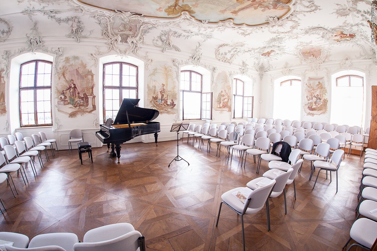 Ein Blick in den Rokokofestsaal von Schloss Leitheim, vorbereitet für ein Konzert mit Flügel und Bestuhlung.