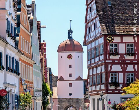 Historisches Königstor mit Uhr zwischen Fachwerkhäusern und bunten Gebäuden bei klarem Himmel.