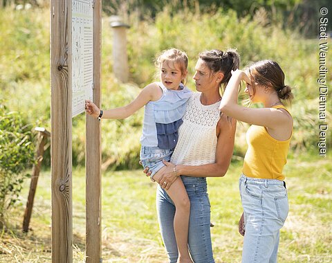 Eine Familie betrachtet eine Informationstafel im botanischen Obstlehrgarten und schafft sich einen Überblick.