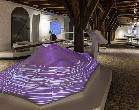 Blick auf ein Modell des Ipfs im Ipf-Museum Modell eines des Berges Ipf mit Projektion von Höhenlinien in einem Museum mit Holzdecke und Steinboden.
