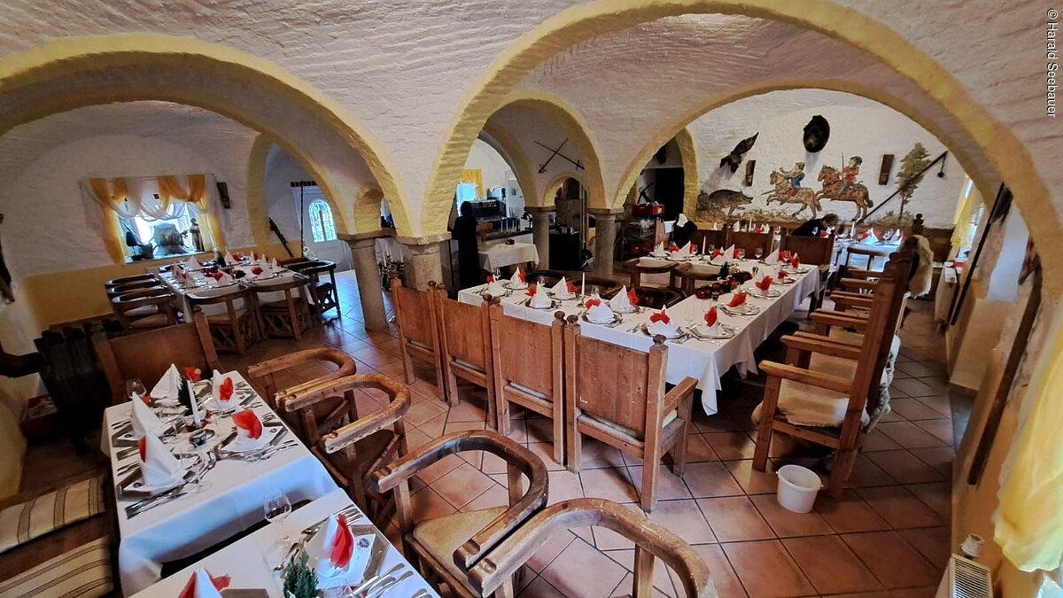 Veranstaltungsräumlichkeit "Kuhstall anno 1559" im Hotel Seebauer Wemding Veranstaltungsraum mit Holzmöbeln, weißen Tischdecken und rot-weißen Servietten unter gewölbten Decken aus Stein.