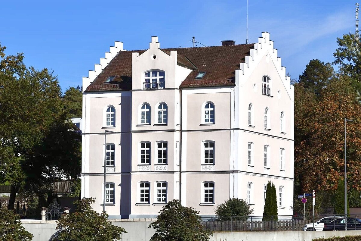 Außenansicht vom Gebäude der Tagungsräume Weise Immobilien GbR Mehrstöckiges weißes Gebäude mit Treppengiebeln und braunem Dach vor blauem Himmel und Bäumen.