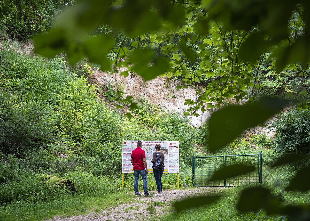 2 Menschen stehen vor der Geopark Ries Tafel des Steinbruchs am Sagenweg bei Wemding.